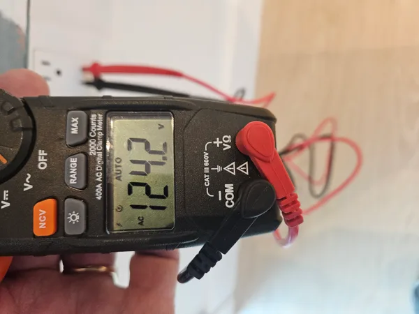 Digital clamp multimeter measuring AC voltage at an electrical outlet during a forensic investigation