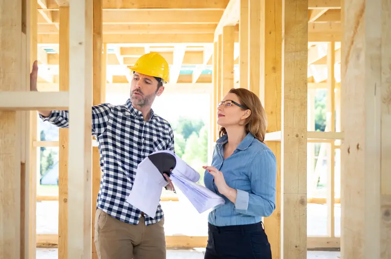 Owner's representative in a hard hat reviewing plans with a building owner inside a wood-framed building under construction